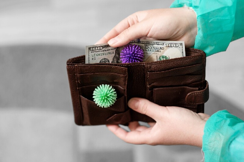 The hands of a healthcare worker holds open a wallet showing a $100 bill and coronavirus particles