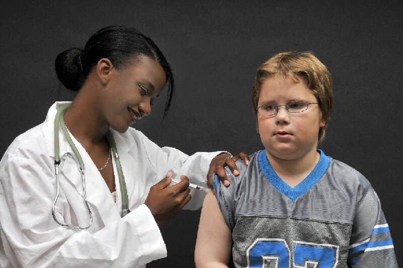African-American female doctor gives a young white male a flu shot in his arm. African-American female doctor gives a young white male a flu shot in his arm.