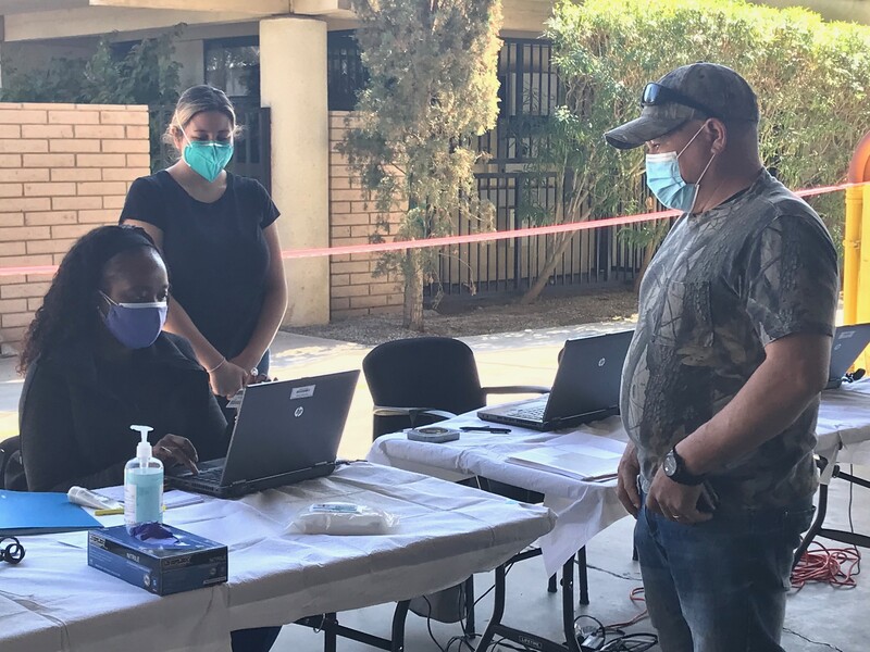 Masked farmworker stands before the registration table manned by two nurses at Anthony Vineyards.