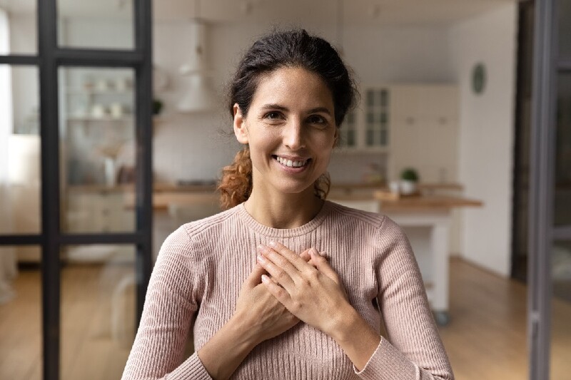 Woman smiling to the camera with both hands placed on her chest in the heart area. Stock Photo