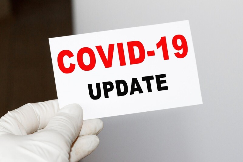 A white gloved hand holds a sign that reads "COVID-19 UPDATE." Stock Photo