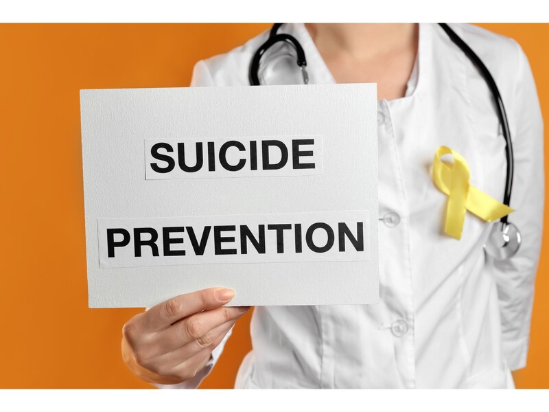 September is National Suicide Prevention Month. Stock Photo. Medical professional in white coat holds a sign that reads "Suicide Prevention." Stock Photo
