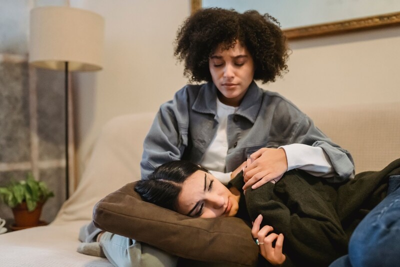A young depressed woman cries as she lays in the lap of a female friend. Stock Photo