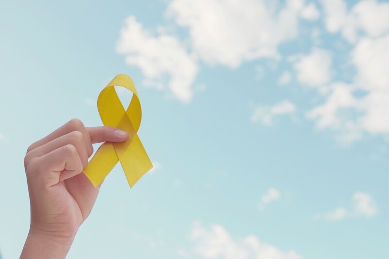 The yellow ribbon symbolizes suicide prevention awareness. Stock Photo A hand holds up a yellow ribbon with a blue sky with white clouds in the background. Stock Photo
