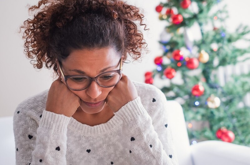 Anxiety and depression can be frequent visitors during the holiday season. Stock Photo An African-American woman holds her head in her hands as she looks down. Stock Photo