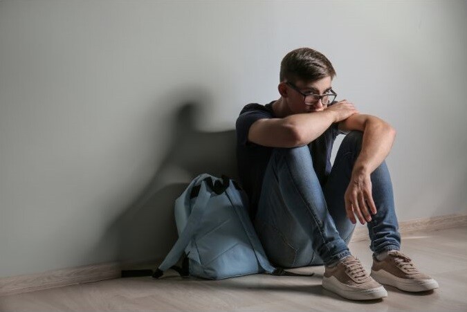 Teen boy with glasses sits on the floor looking despondent. Stock Photo