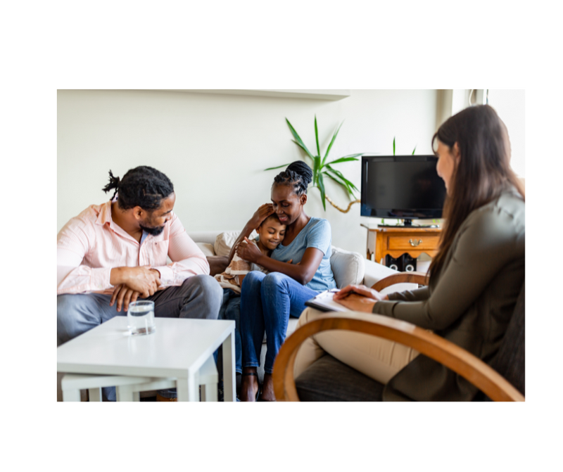A young black couple with a small daughter sits on a sofa facing a seated behavioral health therapist. Stock Photo