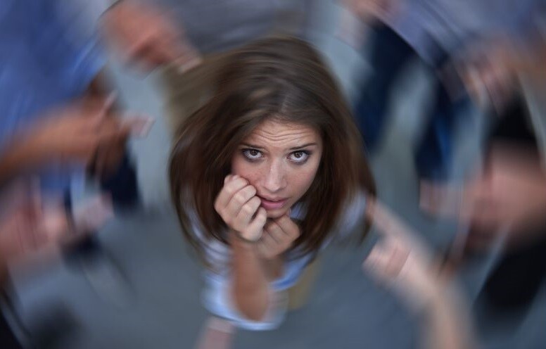 March 2024 is National Self-Harm Awareness Month. Stock Photo A young white woman with shoulder-length brown hair and her hands raised toward her face looks up to the camera as colors swirls around her.