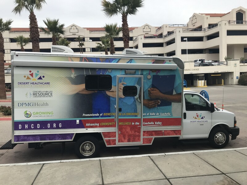 Mobile medical clinic parked in profile (right side) at Desert Regional Medical Center campus with the El Mirador Building in the background.