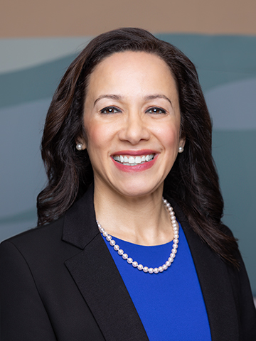 Head shot of her smiling to the camera. She wears her dark hair down. Her outfit consists of a black jacket, royal blue blouse and a pearl necklace and earrings. Submitted Photo