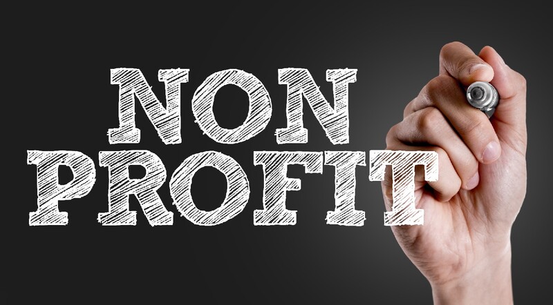 "Non Profit" is printed in white letters on a glass, as we see a hand raised to the word and holding chalk.
