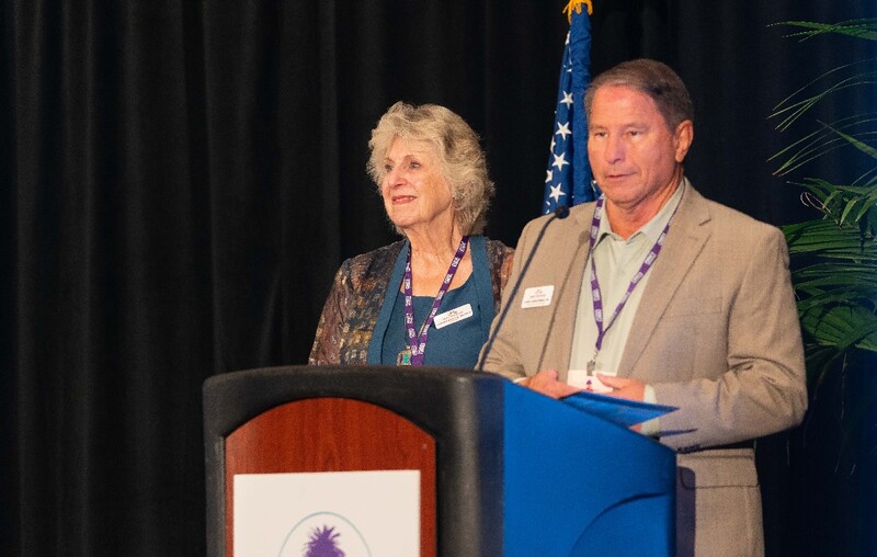 A man and woman standing behind a podium on stage and looking out at an unseen audience. Staff Photo