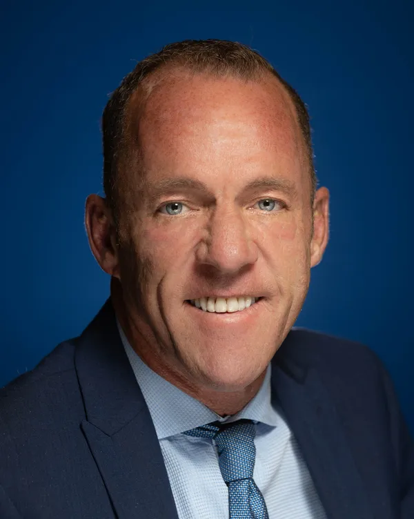 A clean-shaven man with blue eyes and light-brown hair smiling.