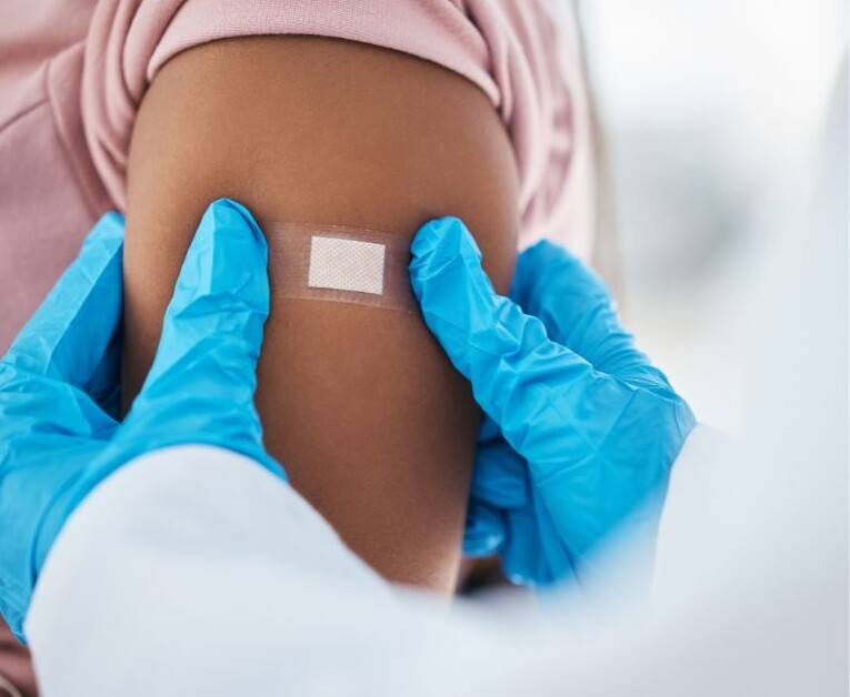 A Band-Aid is applied my a medical professional wearing blue gloves to the arm of a child. Stock Photo